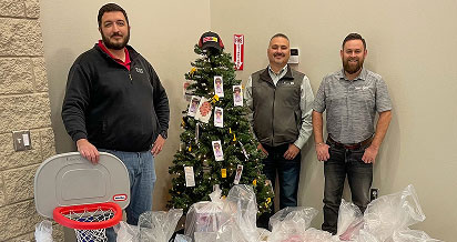 Three men smile in front of Christmas tree